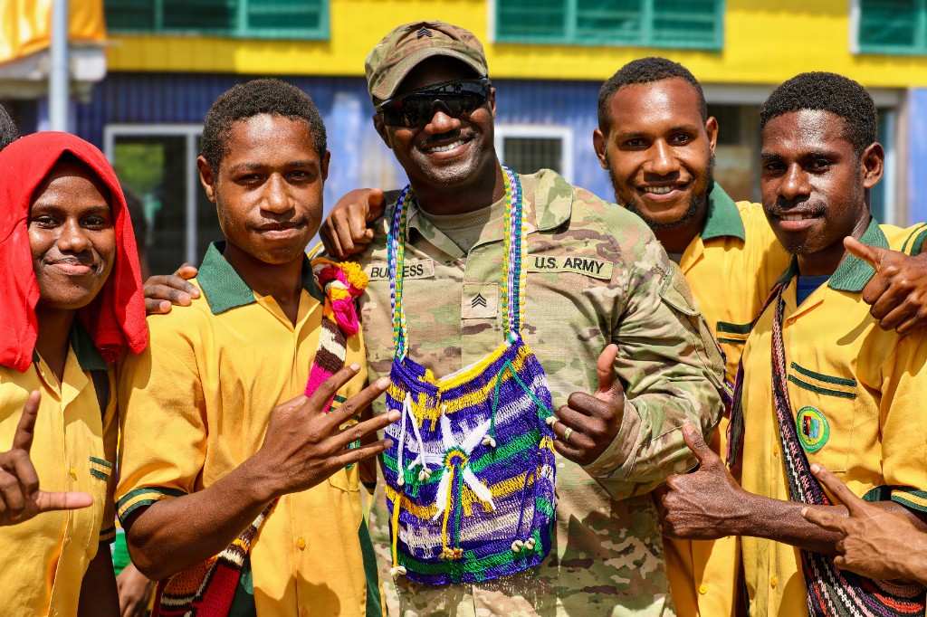 U.S. Army Sgt. Burgess smiles with Papua New Guinean students at Igam Barracks Primary School, wearing a traditional bilum during the Tamiok Strike 26 community celebration
