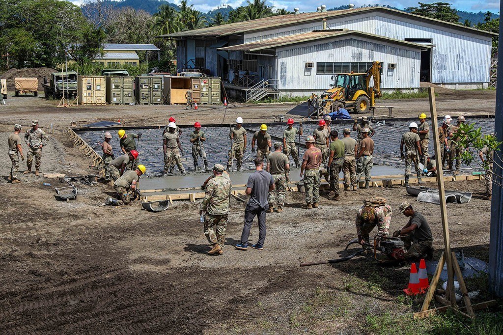 Military personnel pouring and leveling a concrete foundation at a construction site